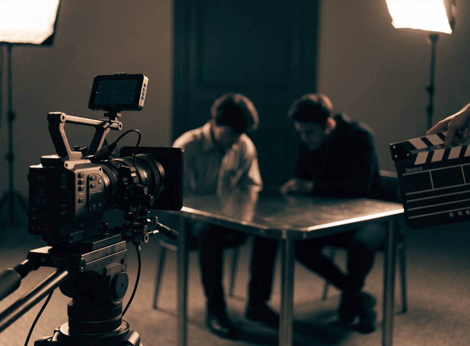 Plan filmowy sceny przesłuchania: kamera na statywie, lampy, klaps, aktorzy przy metalowym stole